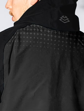 A close-up of a person wearing a black jacket with a subtle cross pattern on the back and a Baselayer logo printed near the hood.