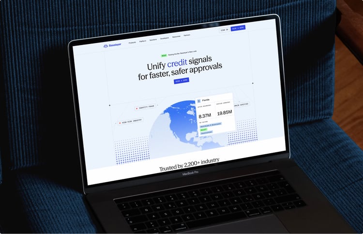 A laptop displaying a webpage with the headline “Unify credit signals for faster, safer approvals,” along with a map graphic and data panels showing business verification information.