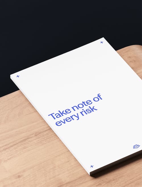 A closed white notebook on a wooden surface with the text “Take note of every risk” printed on the cover.