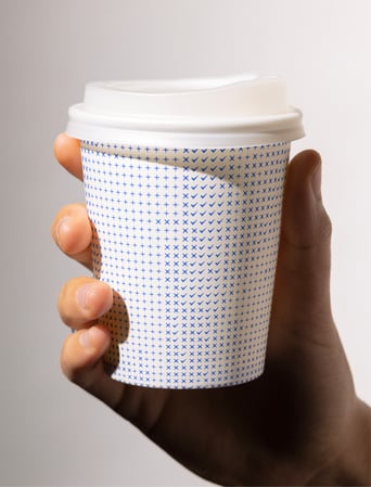 A hand holding a takeaway coffee cup decorated with a blue cross-and-check pattern.